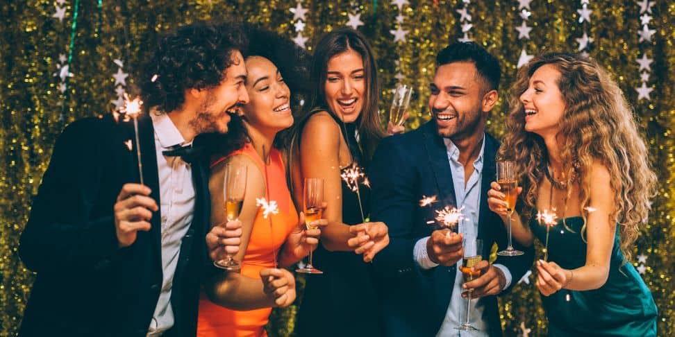 five friends at a new years eve party  holding a drink in one hand and a sparkler in the other