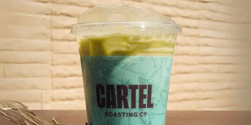 Matcha latte in a plastic cup with the words 'Cartel Roasting Co.' on the cup.