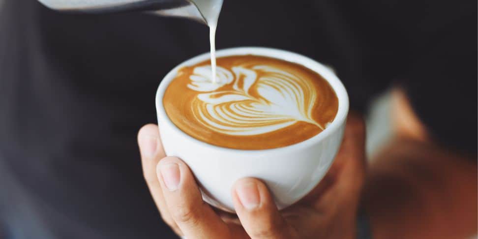 A person pouring milk into a cup of coffee.