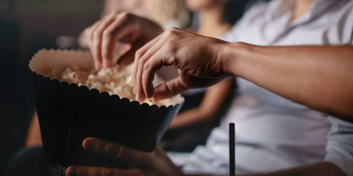 Close up shot of young people eating popcorn in the movie theater, focus on hands.