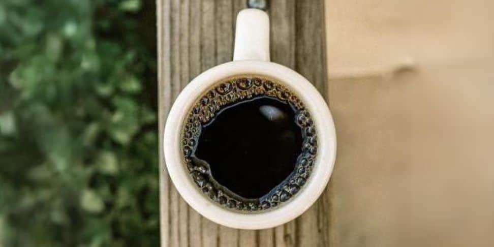 A cup of coffee sitting on a wooden fence.