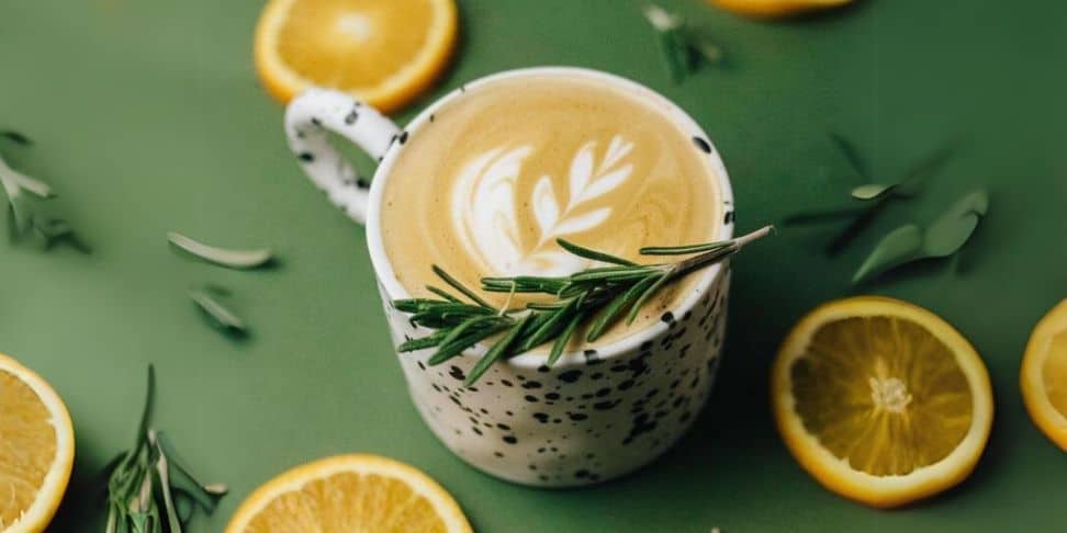A latte surrounded by orange slices and rosemary.