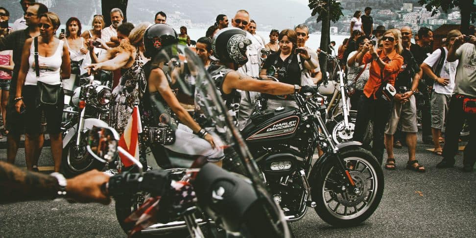 A biker event with riders on motorcycles, viewed from the perspective of a participant, surrounded by an enthusiastic crowd of spectators.