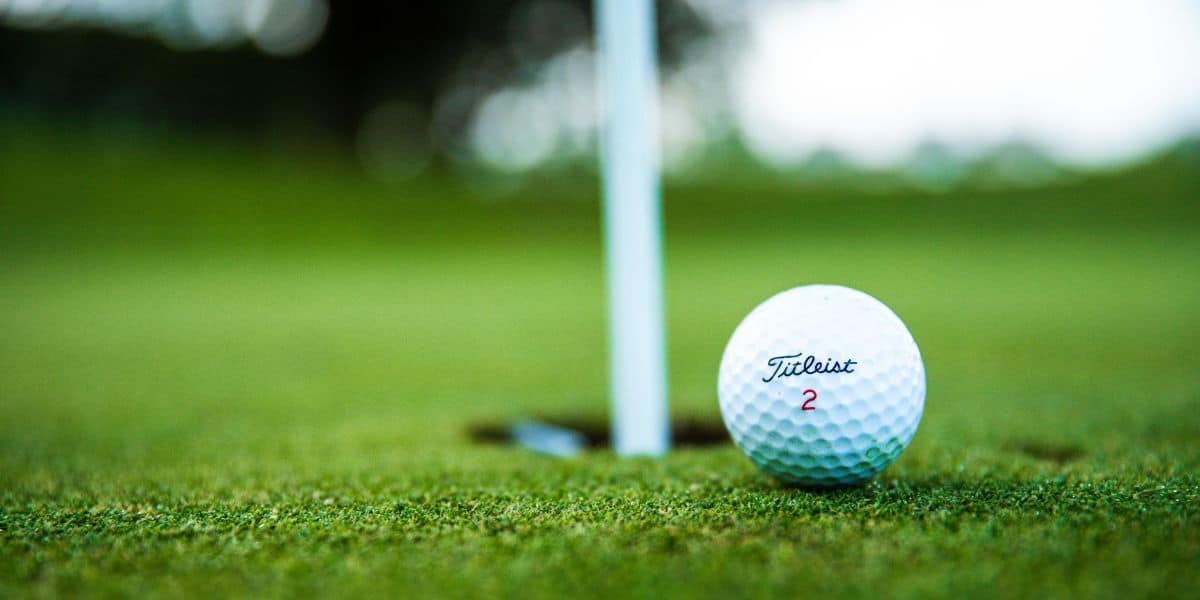 A close-up view of a Titleist golf ball resting on the putting green near the hole, capturing the moment before it is putted in.